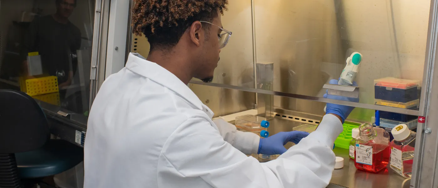 A student in a white lab coat using lab equipment