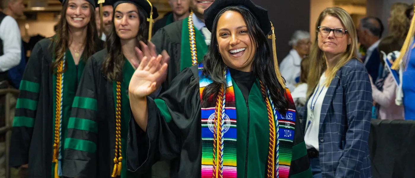 A group of U N E graduate students in black and green wave at the camera