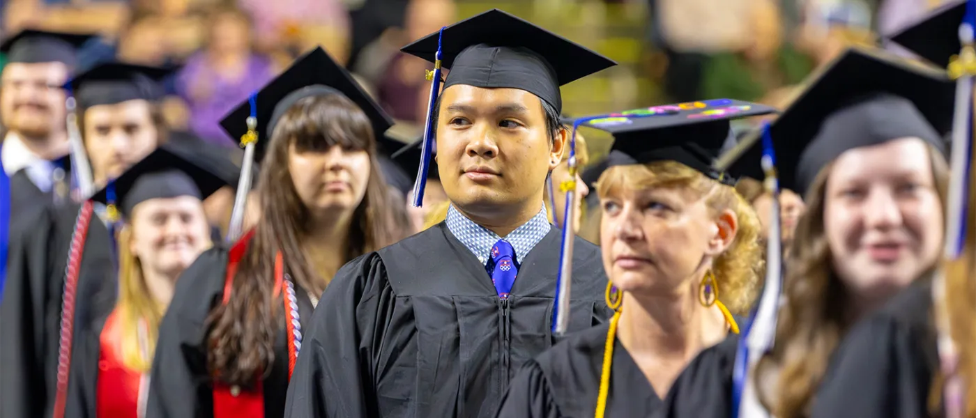 Undergraduate U N E students stand at 2024 commencement before crossing the stage