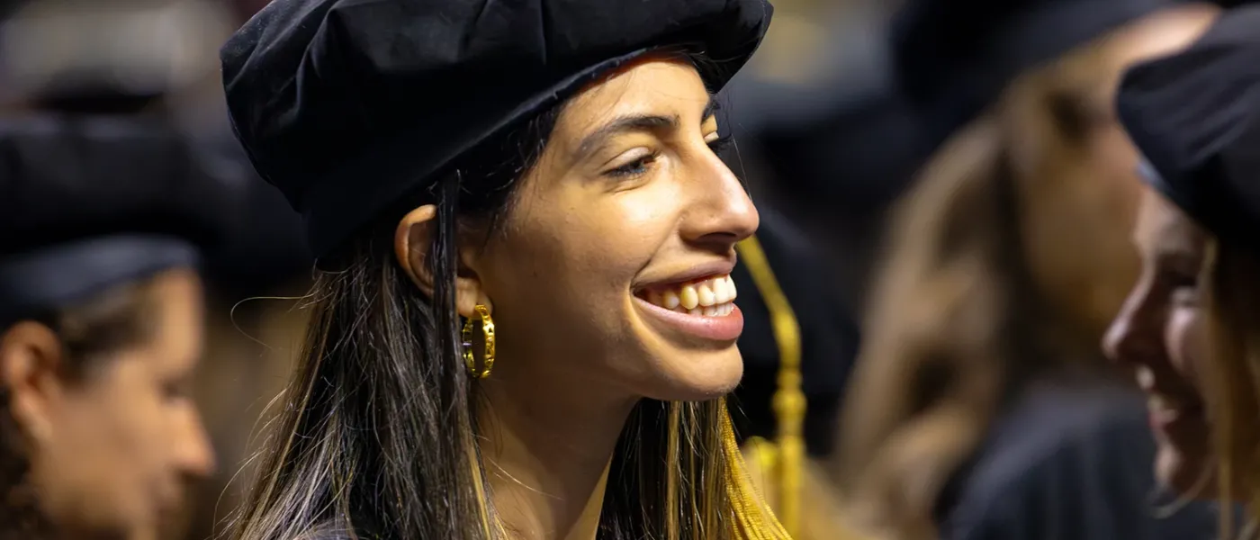 A graduate student in a tam smiles at U N E Commencement