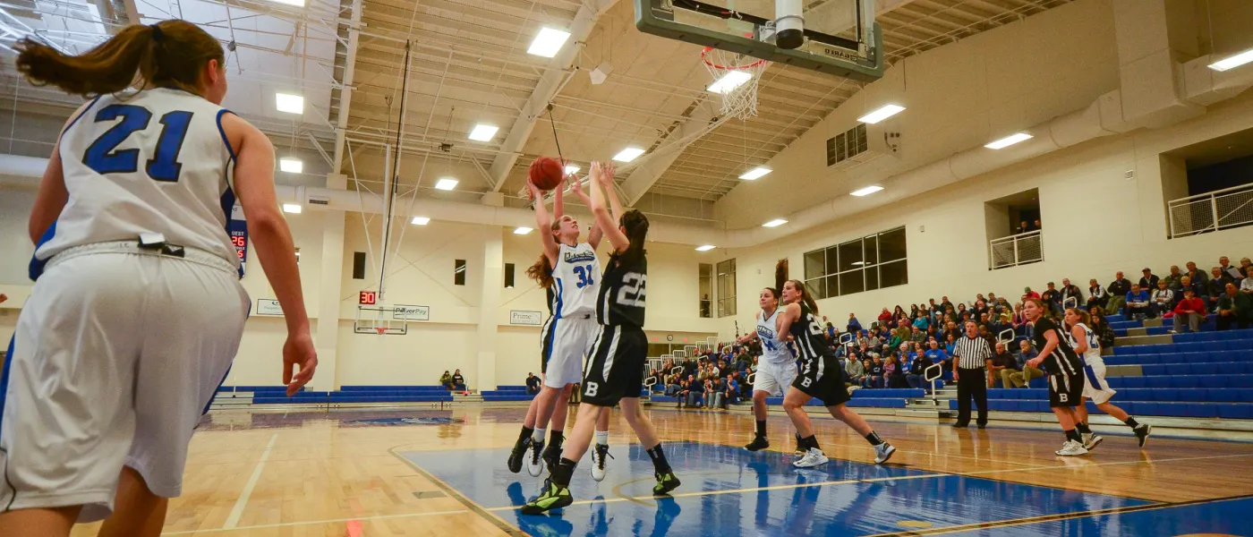 A member of the U N E women's basketball team shoots over the outstretched arms of an opponent