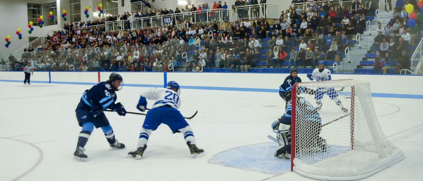 The U N E men's hockey team plays while a large crowd looks on 