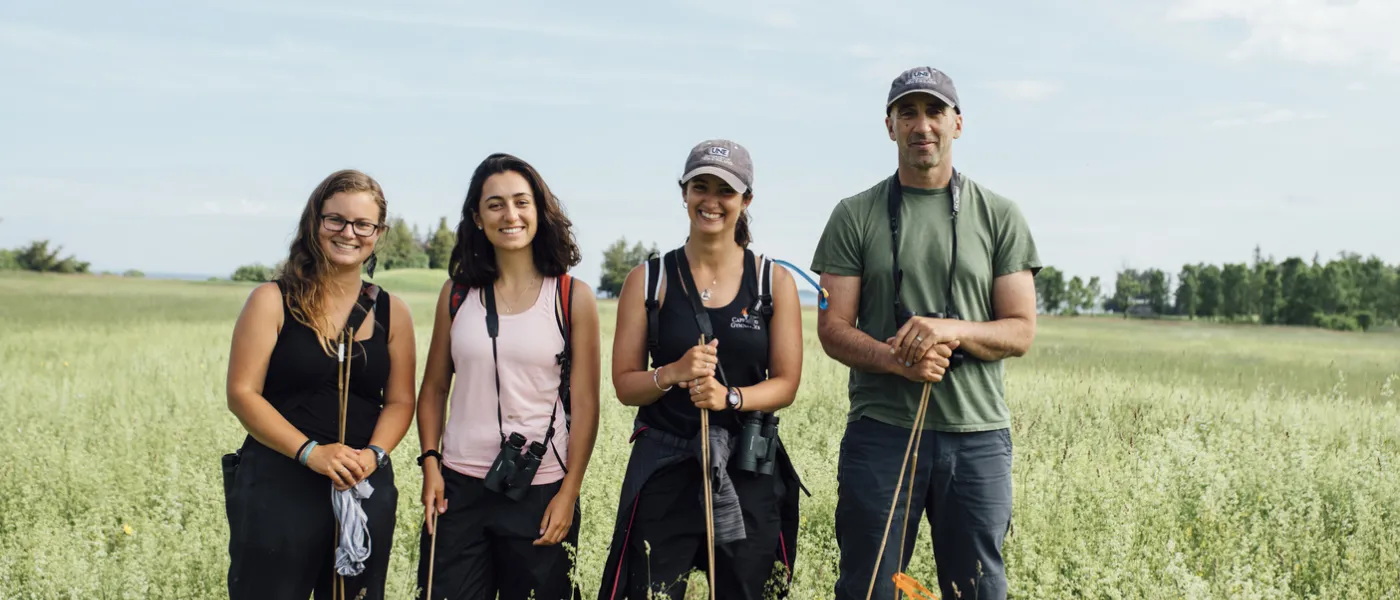 Four U N E researchers stand in a grassy field