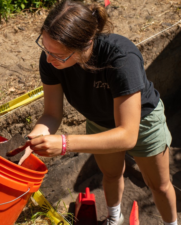 A student brushes dirt off an artifact found in a dig site