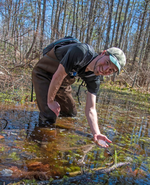 A U N E student holds a mass of frog eggs while standing in a vernal pool