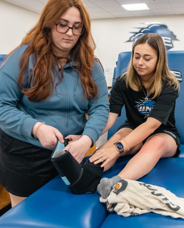 An athletic training student practices wrapping another student's ankle