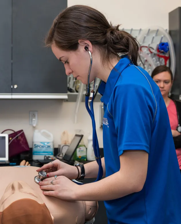 A student uses a stethoscope on a patient simulator