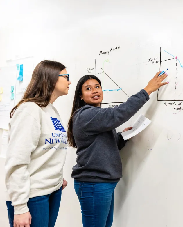 A student explains a drawing of a graph on a whiteboard to another student