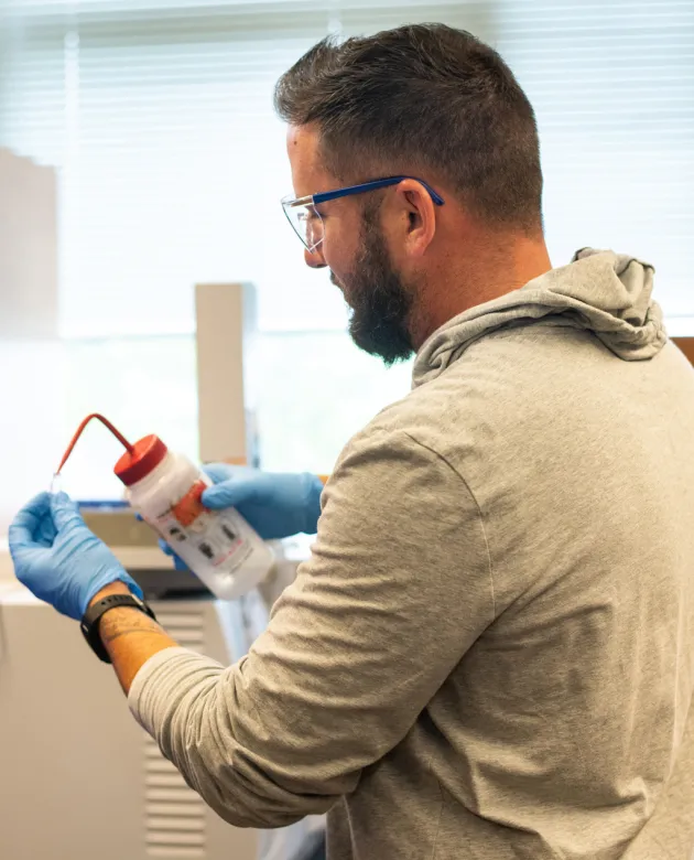 A chemistry student squeezes liquid into a small test tube from a bottle