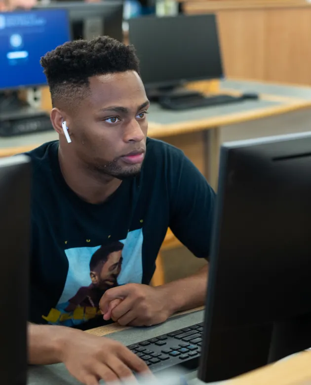 A student sits at a computer in the Biddeford Campus library