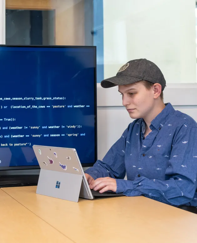 A student works on a coding project on their iPad as it shows behind them on a large monitor