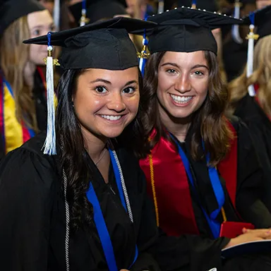 Two College of Arts and Science undergraduate students sitting together at their commencement ceremony