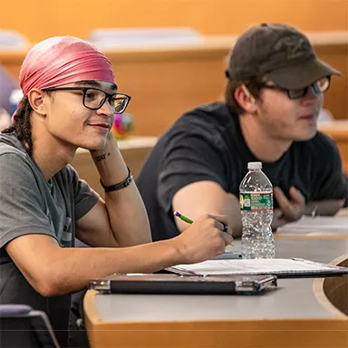 Two U N E students taking notes during a lecture in a lecture hall