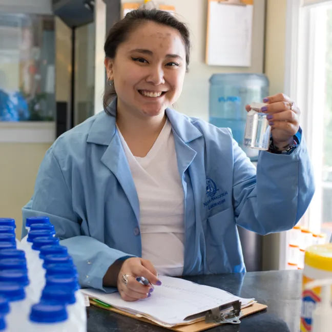 A student smiles as they hold up a small bottle of clear liquid