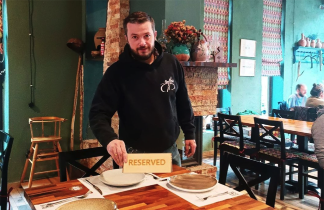 A man poses for a photo while setting the dining table