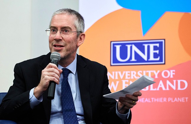 Bryan Caplan holding the microphone and notes in another hand while responding to a question posed by Shannon Zlotkowski