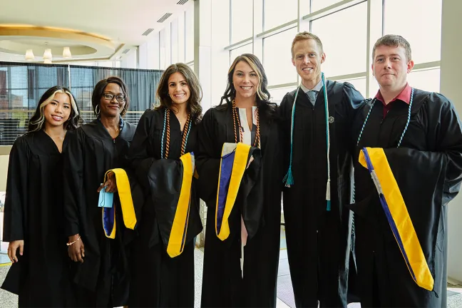 Six graduate students pose in their commencement robes