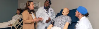 A group of students from different health programs discuss a diagnosis over a patient simulator