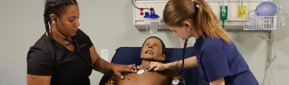 Two P A students practice using stethoscopes on a patient simulators in the sim lab