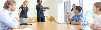 A group of students talk at a table in a bright classroom