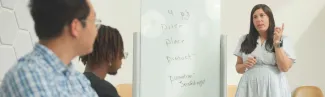 A professor talks to three students in a small classroom