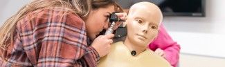 A nursing student uses an otoscope on a patient simulator