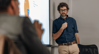 A UNE professor stands against a whiteboard while another professor speaks