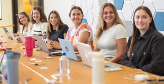 A group of UNE women business students sits around a conference table