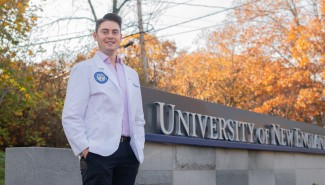 A UNE medical student poses in front of the University's entrance sign