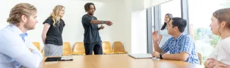 A group of students talk at a table in a bright classroom