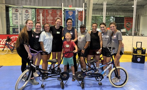 A group of UNE physical therapy students and faculty pose with a child surrounded by bikes 