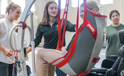 Students help a Maine Adaptive client into a power wheelchair using a lift