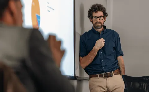 A UNE professor stands against a whiteboard while another professor speaks