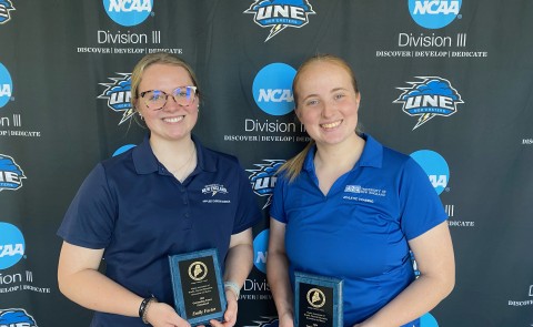 Two female students pose for a photo holding awards