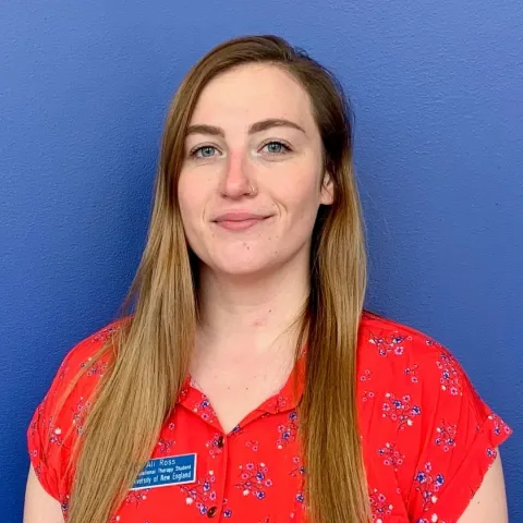 Ali Ross stands smiling against a blue background