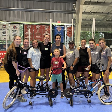 A group of UNE physical therapy students and faculty pose with a child surrounded by bikes 