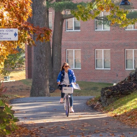 A UNE student bikes through campus in the fall 