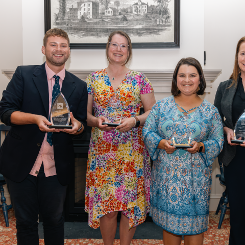 Four members of the Office of Communications pose for a photo in Alumni Hall holding awards