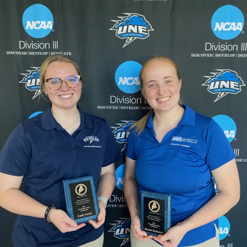 Two female students pose for a photo holding awards