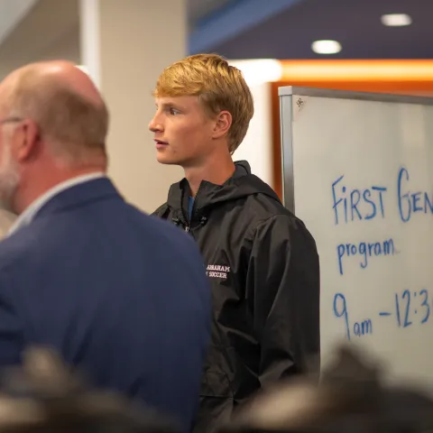 Student stands in front of sign for first-gen orientation.