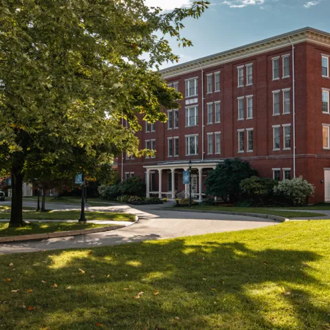 A brick building sits behind green grass and a large tree